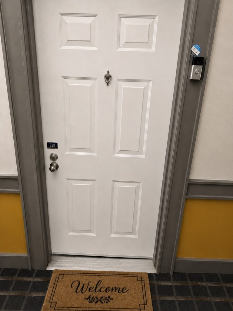 The entrance to Dusten's office: white door numbered 813 with a Welcome mat and a Ring doorbell